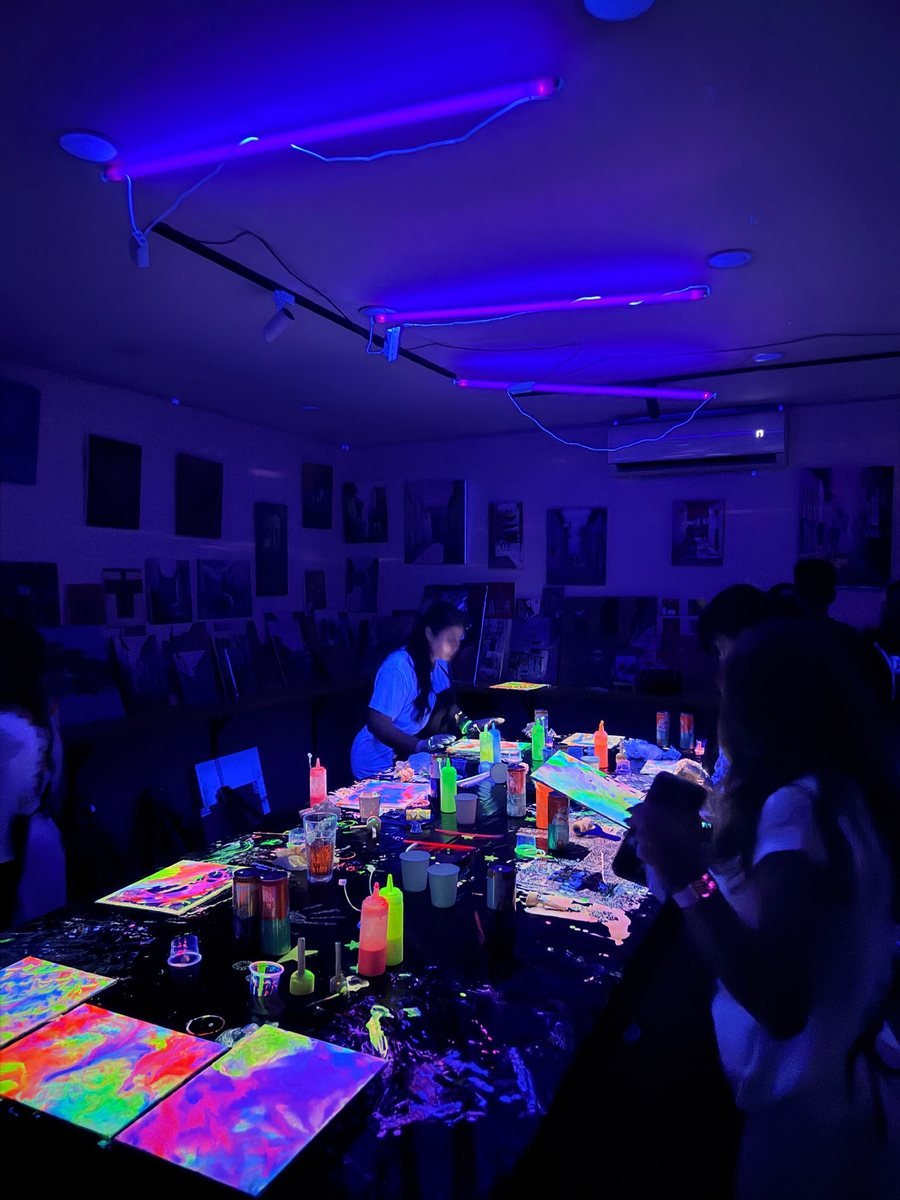The UV-lit table lined with finished neon canvases.