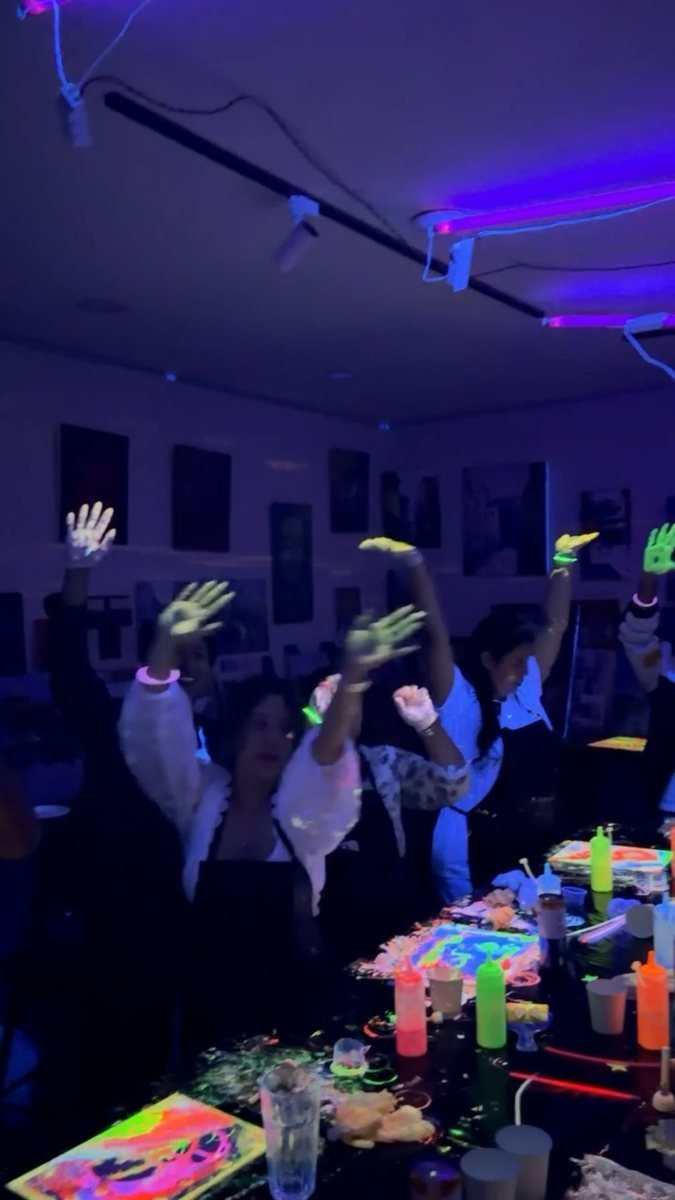 Paint-covered hands thrown up under the UV light.
